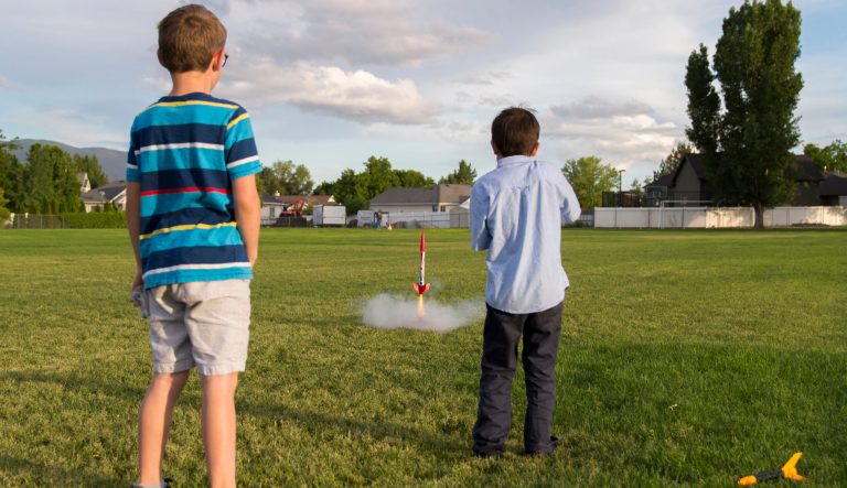 Two boys are launching a model rocket in a large field. 