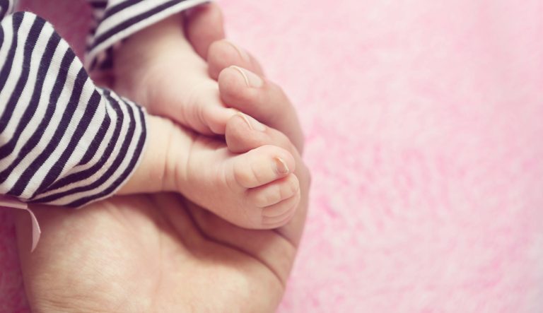 A baby girl's feet being held by her father.