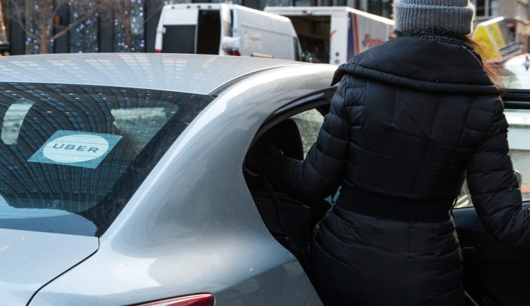 A woman in a black coat is getting inside of a Uber. 