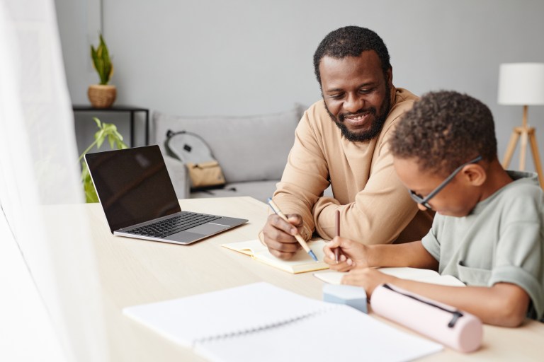 Father helping son with homework while studying at home.