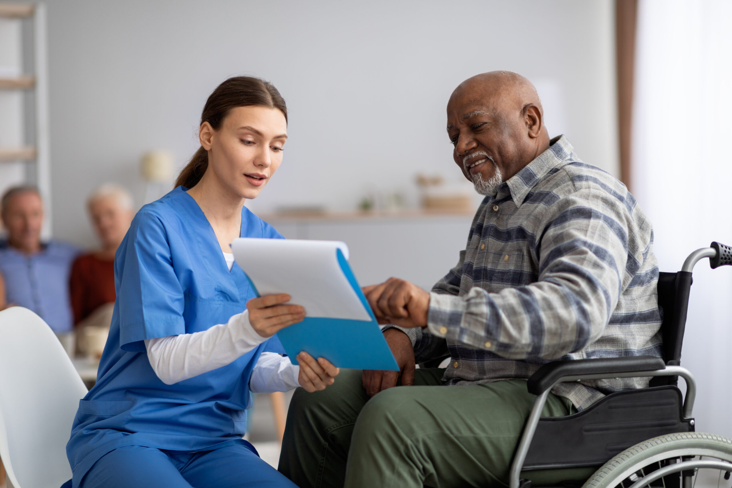A young nurse helps an older black man in a wheelchair with a questionnaire.