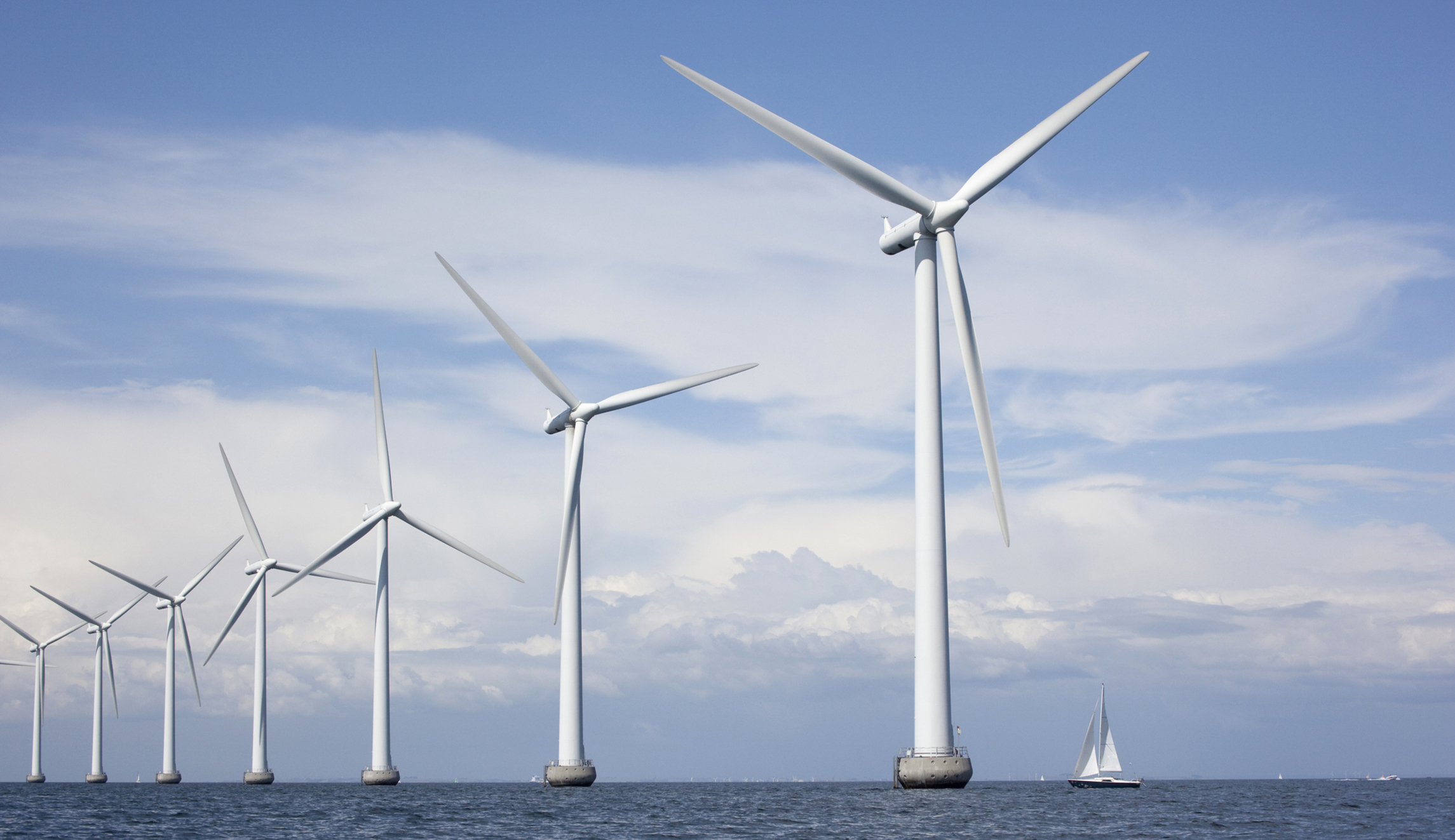 Large white windmills in the sea with a sailboat