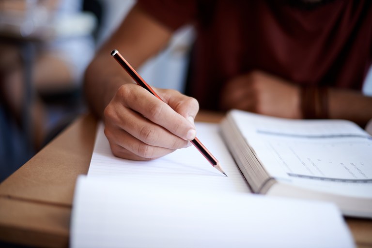 Closeup shot of a young man writing on a note pad.