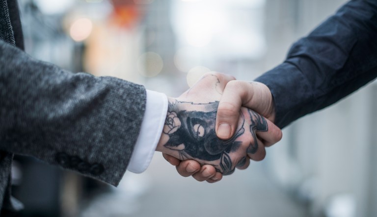 A tattooed businessman shakes hands with a colleague.