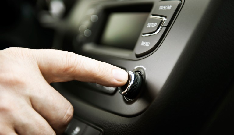 A person presses a button on a car stereo.