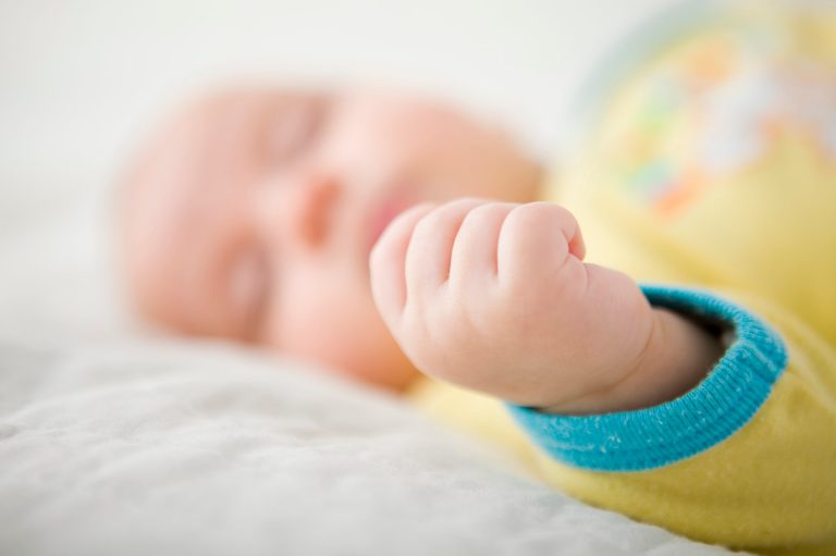 A baby with Down syndrome sleeps on top of a blanket.