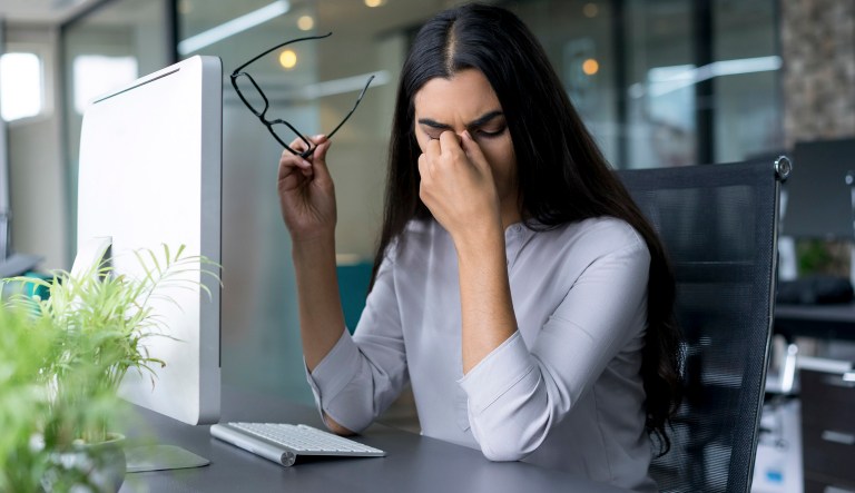 An overworked young businesswoman sits at a computer.