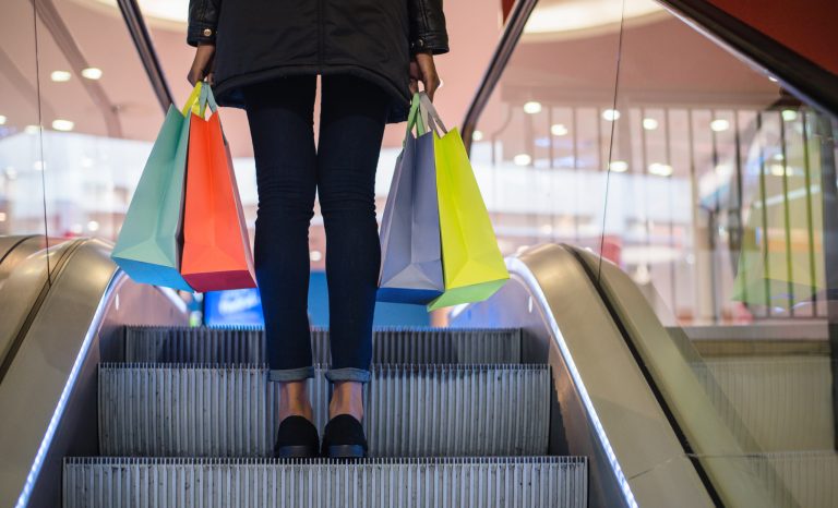 A woman carrying shopping bags on the escalator in a shopping mall.