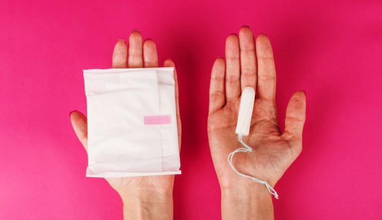 A woman holds a menstrual tampon and pad on a pink background.