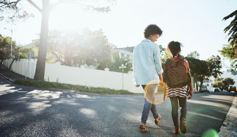 A young mother and her daughter walk down the street together during the day.