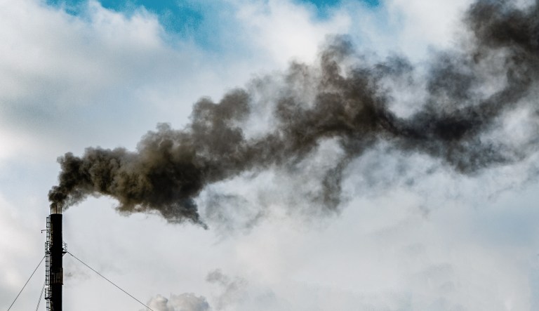 Dark black smoke rises from a factory chimney. 