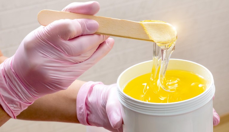 A person holding wax for sugaring in a cosmetic jar at a beauty salon.