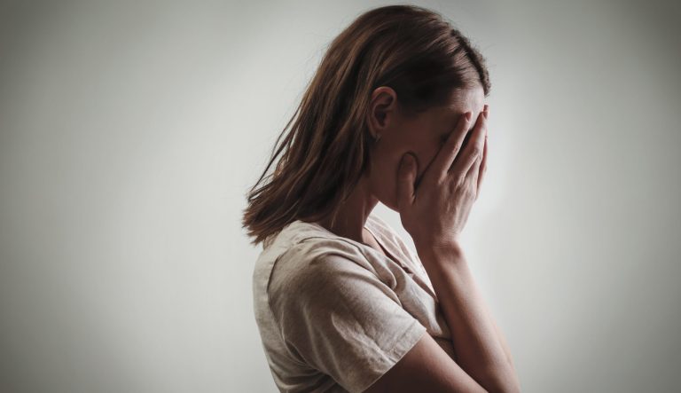 Portrait of a distressed woman, covering her face with her hands.