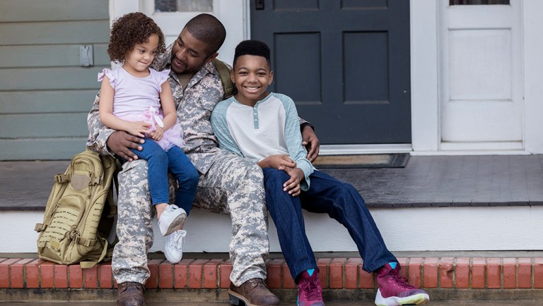 Army dad sits on the porch with his preteen son and preschool age daughter before he leaves for an overseas assignment.