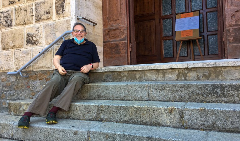 Rev. Lorenzo Pasquotti poses for photos on the steps of his church at the Giglio Island, Italy, Wednesday, June 24, 2020y. Some 50 local mourners filled the pews for that funeral in Saints Lorenzo and Mamiliano Church, including a man from the continent that had COVID-19 infection, recalled the pastor, Rev. Pasquotti. âAfter the funeral, there were greetings, hugging and kissing,â as always. Then came the procession to the cemetery,  where  âthere were more hugs and kisses.â  Yet, ânone of us had any signâ of COVID-19 in the days to follow, said Pasquotti. âNo one was sick. No symptoms that can make you think you were infected.â 