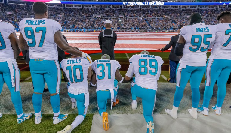 Miami Dolphins' Jordan Phillips (97) stands during the national anthem, but shows support for the protest as he puts an arm on the shoulder of kneeling teammate, Kenny Stills (10), Michael Thomas (31) and Julius Thomas (89) before an NFL football game against the Carolina Panthers in Charlotte, N.C., Monday, Nov. 13, 2017. The Panthers won 45-21.