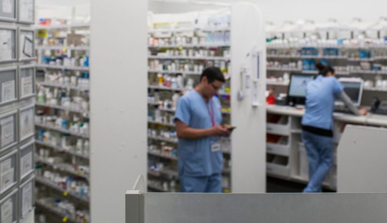 A pharmacist in front of shelves of medication.