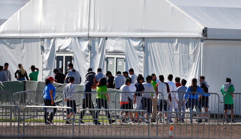 FILE- In this Feb. 19, 2019 file photo, children line up to enter a tent at the Homestead Temporary Shelter for Unaccompanied Children in Homestead, Fla. The company that runs the center is Comprehensive Health Services, which is part of Virginia-based Caliburn International Corporation. 