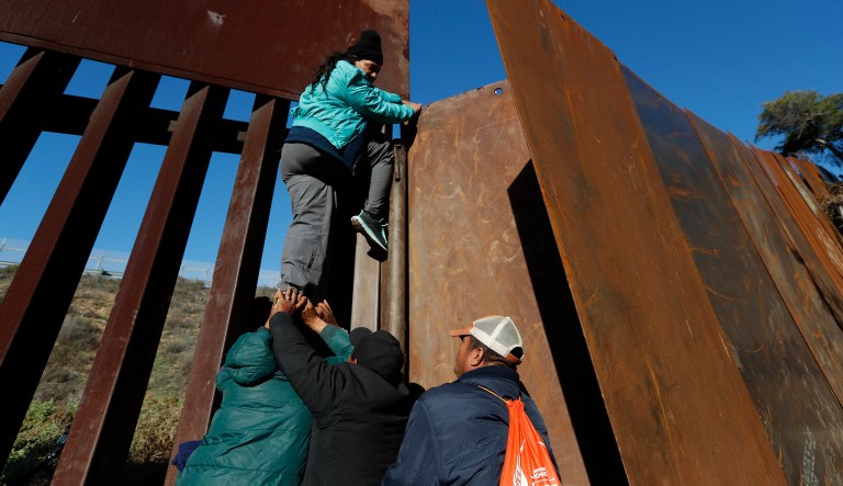 Honduran migrants help a woman cross over the U.S. border wall to San Diego, California, from Playas in Tijuana, Mexico, Wednesday, Dec. 12, 2018. The group of Honduran migrants turned themselves in to U.S. Border Patrol agents in order to apply for asylum.