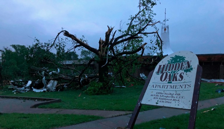 The sign for the Hidden Oaks apartment complex in Jefferson City Missouri stands bent Thursday, May 23, 2019, from a tornado in front of a tree that was ripped apart.