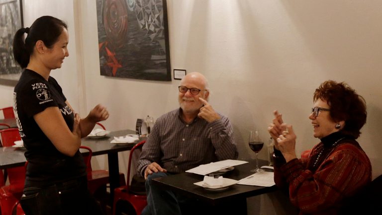 In this Nov. 5, 2015 photo, Mozzeria owner Melody Stein, left, communicates with customers Ronald Ransom and Betty Ann Prinz using sign language in San Francisco. Mozzeria owners Russ and Melody Stein as well as staff workers are deaf and have run their San Francisco restaurant since 2011. 