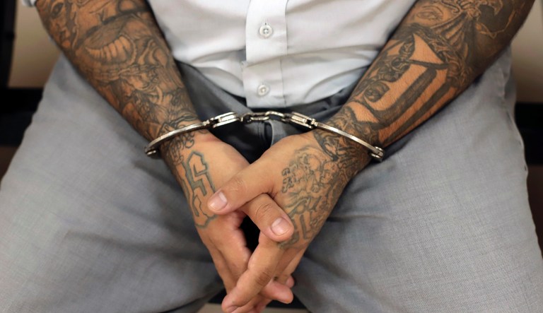 A Mara Salvatrucha gang member with his handcuffed hands shows his tattoos on his arms as he waits for the start of the fourth day of the trial against more than four hundred people connected to criminal gang operations, at the Judicial Center Isidro Menendez in San Salvador, El Salvador, Thursday, Oct. 10, 2019.