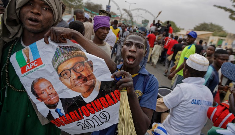 Supporters of Nigeria's President Muhammadu Buhari carry a poster showing Buhari, right, and Vice President Yemi Osinbajo, left, as they march to celebrate his electoral win, on a street in Kano, northern Nigeria Wednesday, Feb. 27, 2019. Buhari on Wednesday defended his sweeping win of a second term as free and fair and appealed to a "common love of country" as his top challenger vowed to go to court with allegations of fraud.