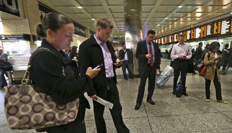 This Thursday, May 9, 2013 photo shows evening rush hour commuters looking at their smart phones while waiting for trains at the Long Island Railroad area inside Penn Station in New York. The busiest passenger train station in the United States, gateway to the biggest city in the nation, is a 1960s-era, utilitarian labyrinth built in what is essentially the basement of Madison Square Garden. Two decades after ambitious plans were unveiled to improve Penn Station while expanding it into the massive Beaux Arts post office building across the street, there are few visible signs of change.