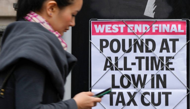 A woman walks past a headline posted on a wall in London, Tuesday, Sept. 27, 2022. The British pound has stabilized in Asian trading after plunging to a record low, as the Bank of England and the British government try to soothe markets nervous about a volatile U.K. economy. The instability is having real-world impacts, with several British mortgage lenders withdrawing deals amid concern that interest rates may soon rise sharply.