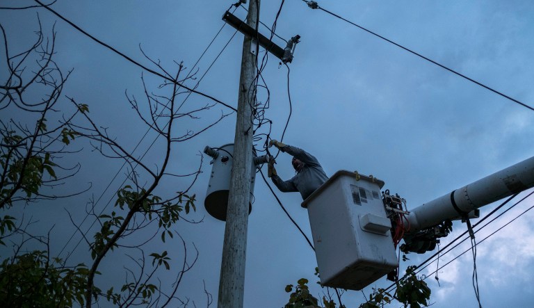 In this July 12, 2018 photo, a laborer from the Puerto Rico Power Authority works to restore power in Adjuntas, Puerto Rico. Puerto Rico's electrical grid is still shaky after Hurricane Irma brushed past the island as a Category 5 storm last Sept. 6 and then Hurricane Maria made a direct hit as a Category 4 storm two weeks later, damaging up to 75 percent of transmission lines.