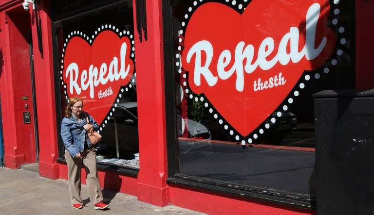 In this May 17, 2018 photo, a woman walks past a "Yes" campaign logo on a shop window in Dublin, Ireland, ahead of the abortion referendum on Friday, May 25.  An abortion debate that has inflamed passions in Ireland for decades will come down to a single question on Friday: yes or no? The referendum on whether to repeal the country's strict anti-abortion law is being seen by anti-abortion activists as a last-ditch stand against what they view as a European norm of abortion-on-demand, while for pro-abortion rights advocates, it is a fundamental moment for declaring an Irish woman's right to choose.