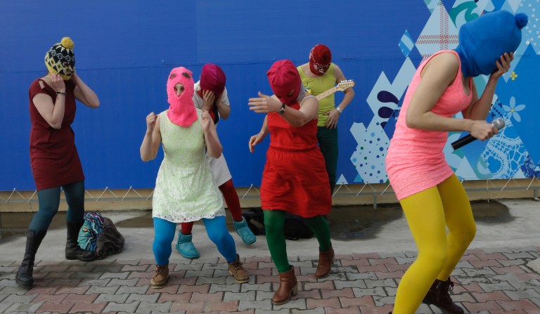 Nadezhda Tolokonnikova covers her face to protect herself from a Cossack militiaman while she and fellow members of the punk group Pussy Riot, including Maria Alekhina, second left, in the pink balaclava, stage a protest performance in Sochi, Russia, on Wednesday, Feb. 19, 2014. 