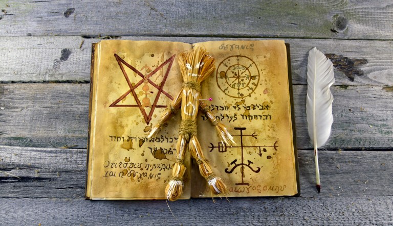 Halloween still life with the black magic book and the doll body made of straw.