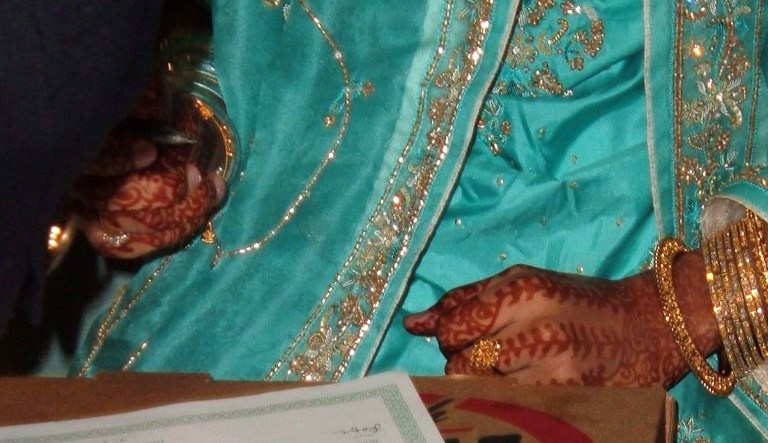 A bride's henna-decorated hands are shown as she is about to sign her marriage contract.