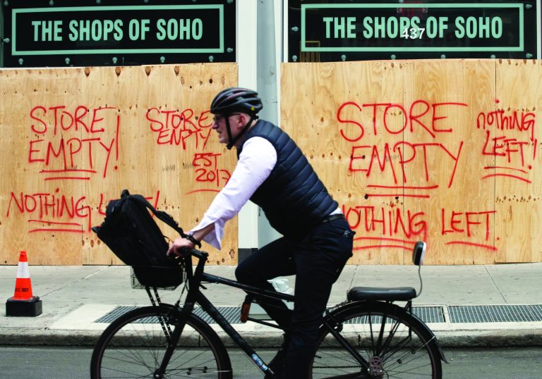 A cyclist passes the Shops of Soho on June 3, 2020 in New York. Graffiti on the boarded up store reads "Store Empty! Nothing Left!"