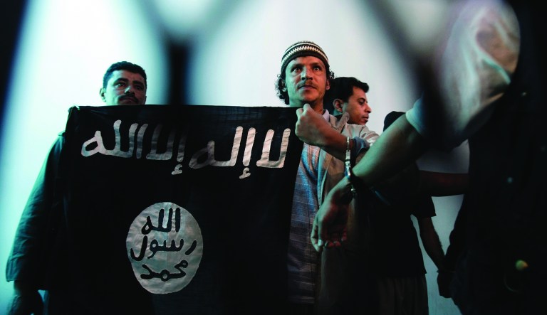 A suspected Yemeni al Qaeda militant, center, holds a banner as he stands behind bars during a court hearing in state security court in Sanaa, Yemen. 