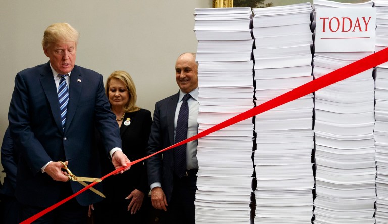 President Trump cuts a ribbon during an event on federal regulations in the Roosevelt Room of the White House, Thursday, Dec. 14, 2017, in D.C. "Let's cut the red tape, let's set free our dreams," Trump said as he symbolically cut a ribbon on stacks of paper representing the size of the regulatory code.