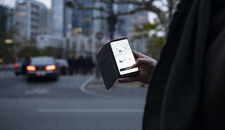 A customer uses the Uber Technologies Inc. Uber X smartphone app as skyscrapers stand in the 'Mainhattan' financial district beyond in Frankfurt, Germany,  on Friday, April 12, 2019.