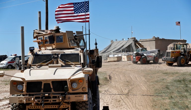 A U.S. soldier, left, sits on an armored vehicle behind a sand barrier at a newly installed position near the tense front line between the U.S-backed Syrian Manbij Military Council and the Turkish-backed fighters, in Manbij, north Syria, Wednesday, April 4, 2018. A week ago, there was just a single house where U.S. soldiers had hoisted a U.S. flag on a hill a little ways back from a tense front line in Syria. Now on Wednesday stood a growing outpost with a perimeter of large sand barriers and barbed wire, a new watch tower and half a dozen armored vehicles, The Associated Press found.