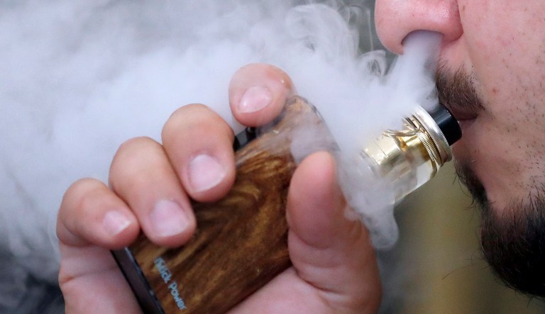 A man breathes vape from an e-cigarette at a vape shop in London, Friday, Aug. 17, 2018.