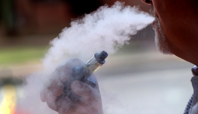 In this Aug. 28, 2019, photo, a man exhales while using an e-cigarette in Portland, Maine. Efforts to ban flavored e-cigarettes and reduce their appeal to youngsters have sputtered under industry pressure in over a half-dozen states this year.