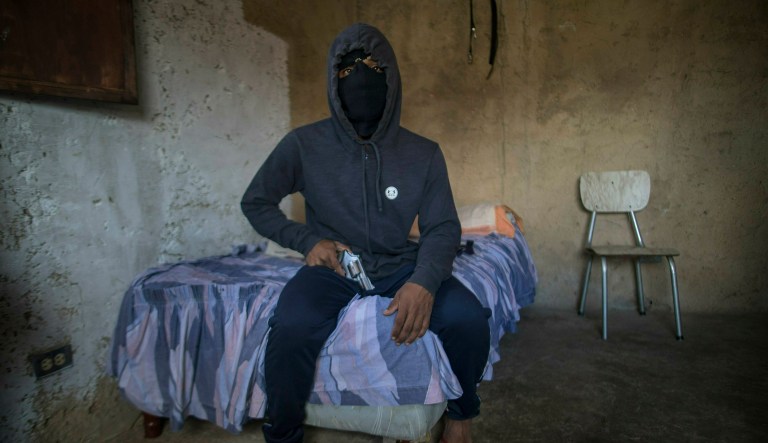 A masked gangster who goes by the nickname "El Negrito" poses for a portrait with his gun inside his gang's safe-house in the Petare slum of Caracas, Venezuela, Monday, May 13, 2019.