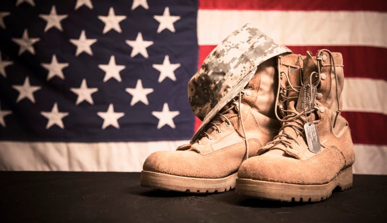 USA military boots, hat and dog tags with American flag in background.  