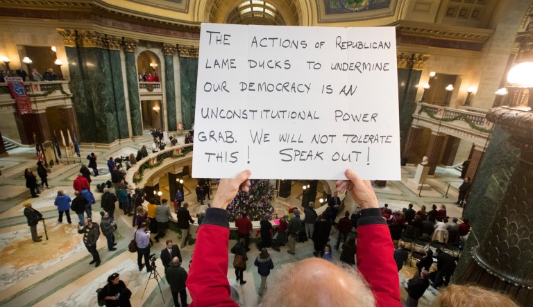 People protest the legislature's extraordinary session during the official Christmas tree lighting ceremony at the Capitol in Madison, Wis., Tuesday, Dec. 4, 2018. Demonstrators booed outgoing Wisconsin Gov. Scott Walker on Tuesday during the Christmas tree-lighting ceremony, at times drowning out a high school choir with their own songs in protest of a Republican effort to gut the powers of his Democratic successor.