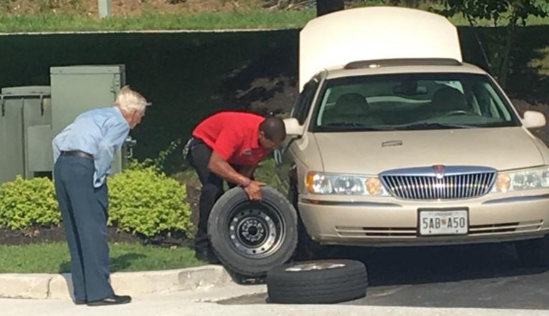 A Chick-fil-A manager (right) helps a WWII veteran (left) change a tire.
