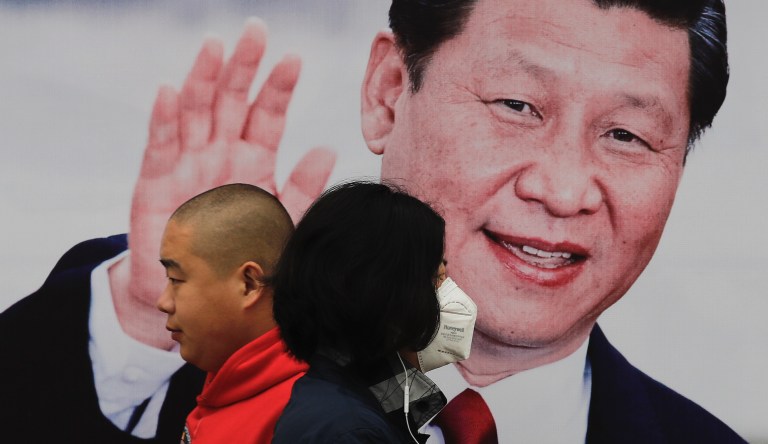 Pedestrians, one wearing a mask, walk by a poster of Chinese President Xi Jinping on a street in Beijing, Thursday, Oct. 26, 2017.
