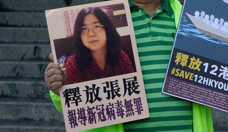 A pro-democracy activist holds placards with the picture of Chinese citizen journalist Zhang Zhan outside the Chinese central government's liaison office, in Hong Kong, Monday, Dec. 28, 2020. Zhang, a former lawyer and citizen journalist from Shanghai, has been sentenced to four years in prison for her reporting on the initial coronavirus outbreak in Wuhan, China. The activists demand the releases of Zhang, as well as the 12 Hong Kong activists detained at sea by Chinese authorities.