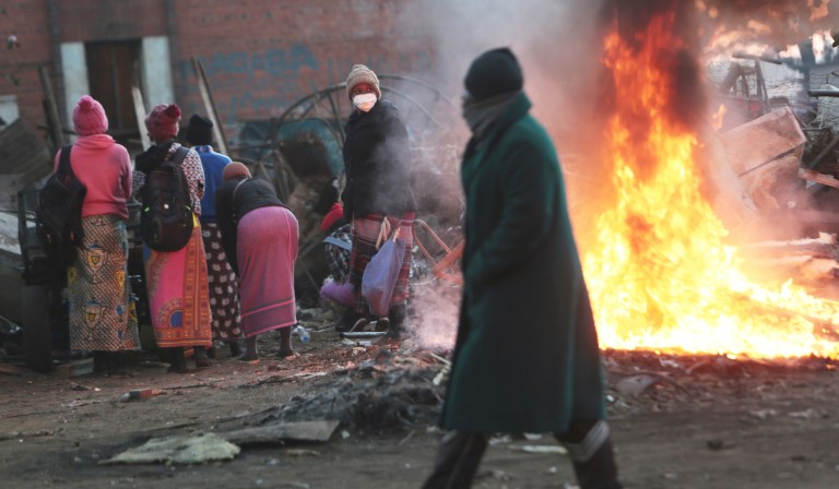 A  man walks past a burning fire   in a poor neighborhood in Harare, Monday, July,20, 2020. The Meterological  Services Department  has warned Zimbabwe to brace for an increase in Covid-19   and other respiratory  diseases during the winter season which the country is experiencing at the moment.The government announced  it would  tighten lockdown measures in light of spiking  Covid-19 cases across the country.(
