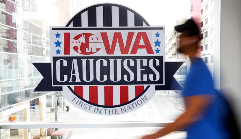 In this Feb. 4, 2020, file photo, a pedestrian walks past a sign for the Iowa Caucuses on a downtown skywalk, in Des Moines, Iowa. The Iowa Democratic Party is agreeing to recount the results in about two dozen of almost 1,700 precinct caucuses as part of the ongoing process to resolve the weeks-long question of who won Iowa's tarnished presidential caucuses. Campaign officials for former South Bend Mayor Pete Buttigieg and Vermont Sen. Bernie Sanders asked for a combined 23 precincts to be recounted. (AP Photo/Charlie Neibergall, File)