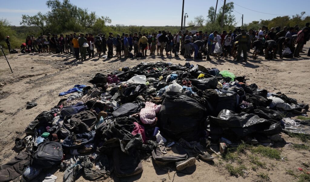 Migrants stands near a pile of discarded items as they wait to be processed by the U.S. Customs and Border Patrol after they crossed the Rio Grande and entered the U.S. from Mexico, Thursday, Oct. 19, 2023, in Eagle Pass, Texas. Starting in March, Texas will give police even broader power to arrest migrants while also allowing local judges to order them out of the U.S. under a new law signed by Republican Gov. Greg Abbott. (AP Photo/Eric Gay)